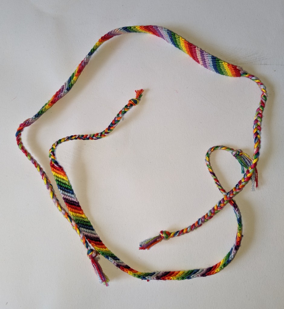 This overhead shot shows two friendship bracelets that show the front and back of the bracelets. Both are rainbow diagonal going from left to right.